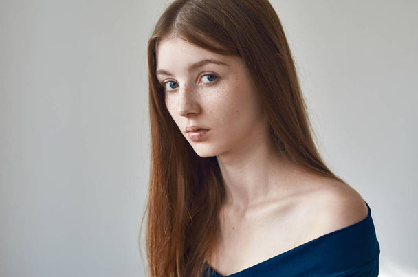 Beauty theme: portrait of a beautiful young girl with freckles on her face and wearing a blue dress on a white background in studio - 写真・画像