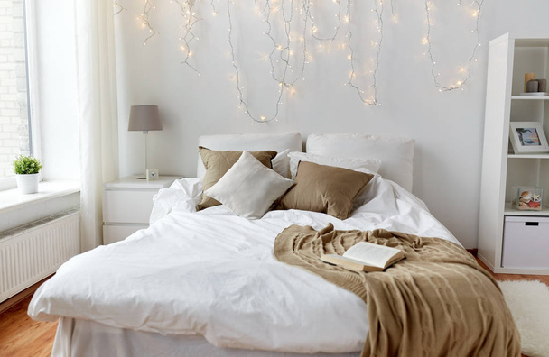 bedroom with bed and christmas garland at home - Фото, изображение