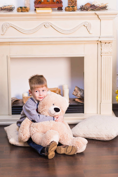 Дитячий хлопчик грає з м'яким іграшковим ведмедем під ялинкою
. - Фото, зображення