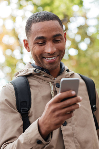Cheerful young african man holding cellphone in hands and chatting - Photo, image