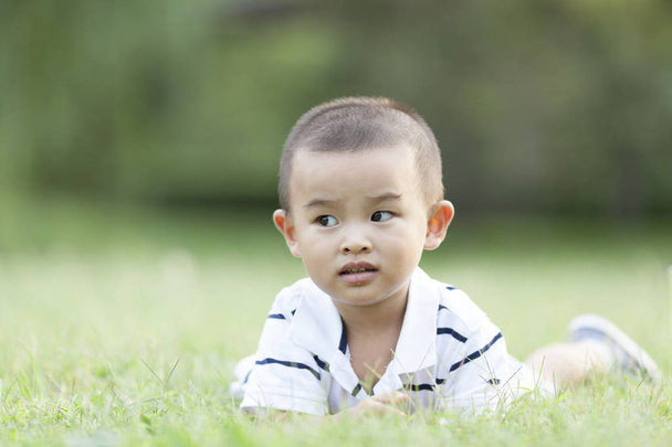 Niño chino feliz acostado en el prado
 - Foto, Imagen