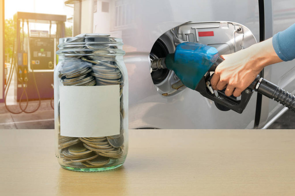 Botella de dinero con monedas, Mano sosteniendo la boquilla de combustible vertiendo
 - Foto, Imagen