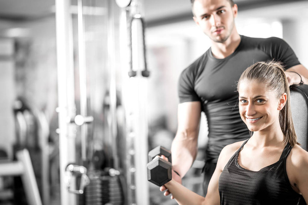 Woman doing bicep curls in gym with her personal trainer - Foto, afbeelding