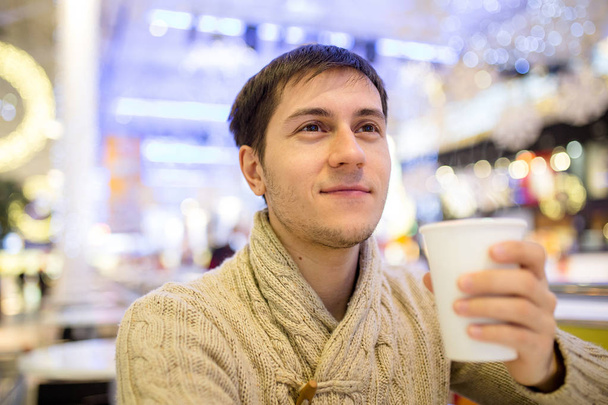 Young happy smiling man holding a cup of coffee in cafe in shopp - Foto, immagini