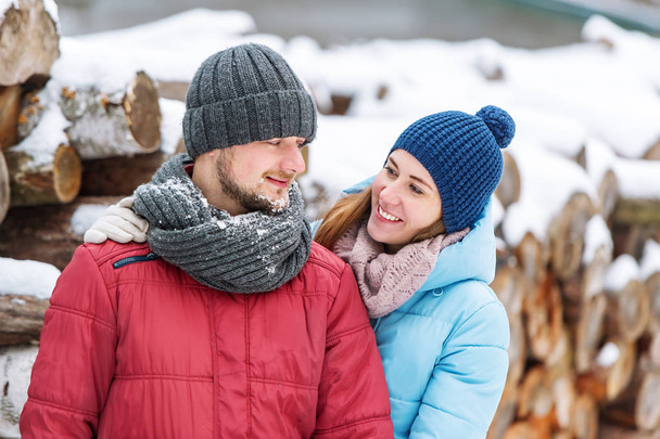 Portrait of young couple in the winter wood. At a background wooden logs lie. - Photo, Image