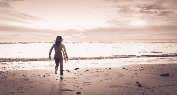 girl dressed in a wetsuit runs on the beach - Photo, Image