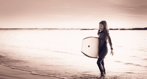 girl dressed with a wetsuit walking on the beach - Photo, Image