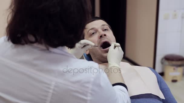 Dentist checks teeth of male patient by dental mirror - Filmati, video