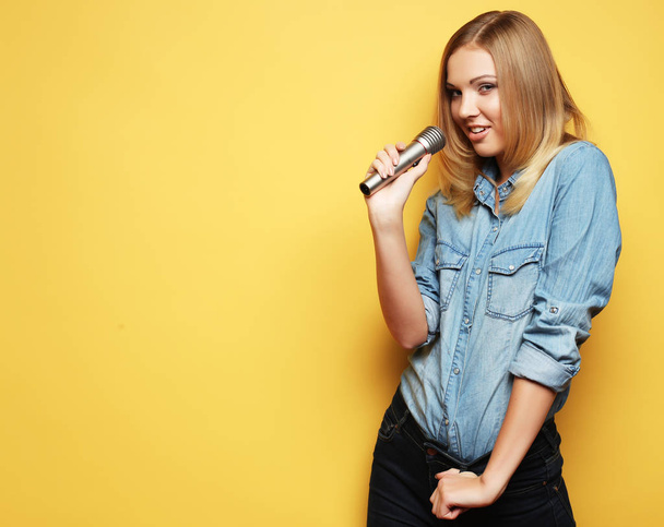 mooie blonde vrouw zingen met microfoon in studio over yel - Foto, afbeelding