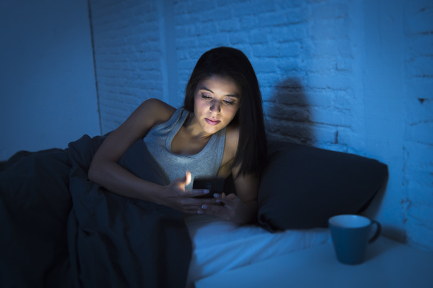 cep telefonuyla gece geç saatte mutlu ve rahat yalan karanlık yatak odası yatakta kız - Fotoğraf, Görsel
