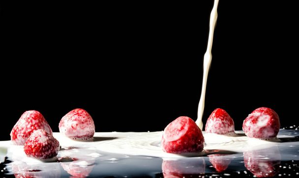 Strawberry Making A Splash. Isolated on black background. Macro photo of a strawberry in milk splashes and drops - 写真・画像