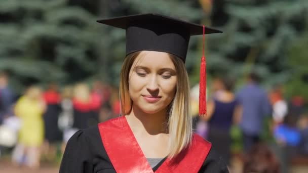 Όμορφη νεαρή γυναίκα σε ακαδημαϊκό ντύσιμο ψάχνει για φωτογραφική μηχανή, επιτυχημένη απόφοιτος - Πλάνα, βίντεο