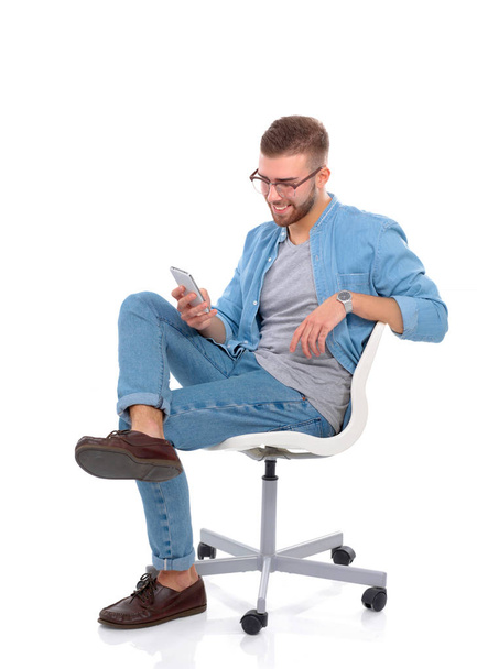 Young man sitting on chair and using mobile phone - Фото, зображення