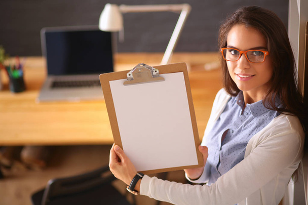 Young woman standing near desk with laptop holding folder - Valokuva, kuva