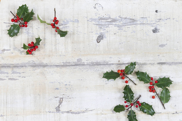 Kleurrijke traditionele kerst Hulst met rode bessen op grunge houtstructuur verweerde van oude planken copyspace - Foto, afbeelding