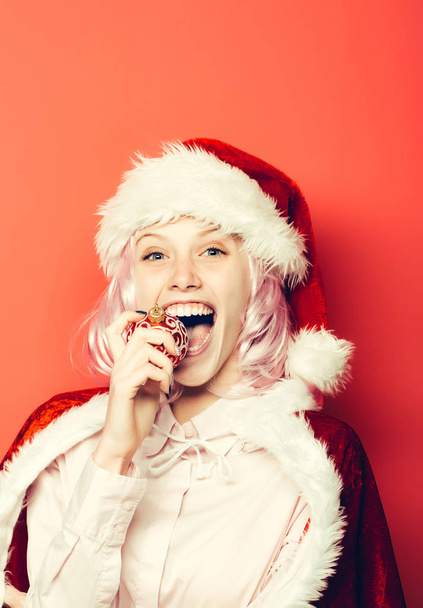 Cheerful girl bites Christmas bauble - Zdjęcie, obraz