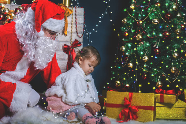 Santa and girl playing near fireplace, decorated Christmas tree - Zdjęcie, obraz