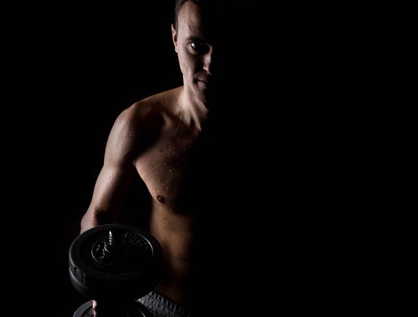 Handsome athletic man with dumbbell on a darck background - Фото, изображение
