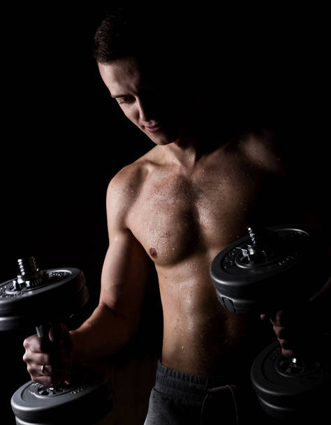 Handsome athletic man with dumbbell on a darck background - Фото, зображення