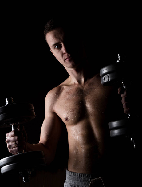 Handsome athletic man with dumbbell on a darck background - Zdjęcie, obraz