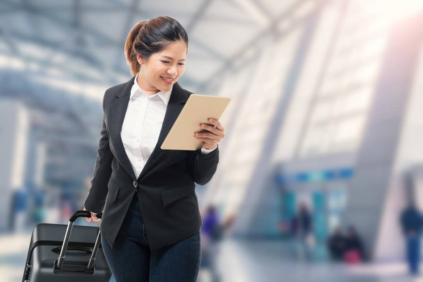 Geschäftsfrau hält Tablet in der Hand, während sie Gepäck trägt - Foto, Bild