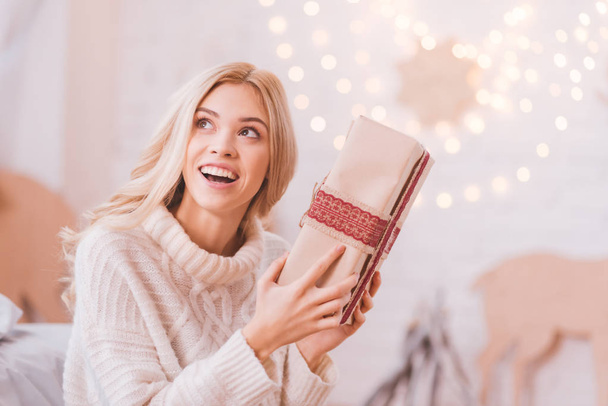 Cheerful curious woman shaking a Christmas box - Fotografie, Obrázek