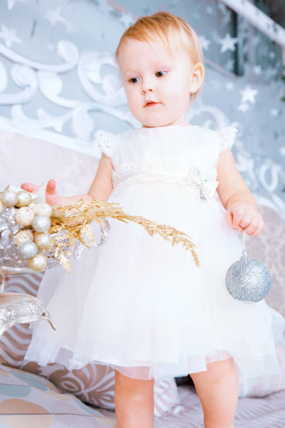 happy little girl in white dress decorates tree in the Christmas decorated room - Foto, Imagem