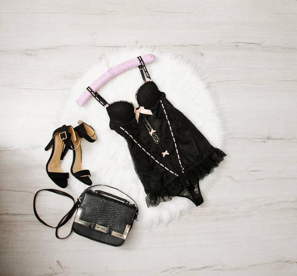 Black lace corset, shoes and handbag on a white fur. Fashionable concept, top view - Photo, Image