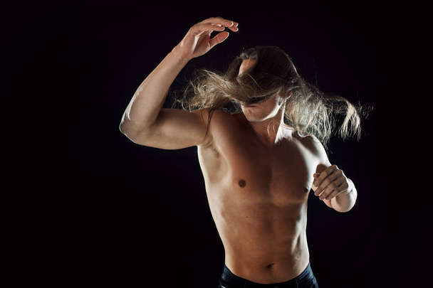 Fighting muscular man with long hair, clasps hands in fist, black background - Foto, Imagem