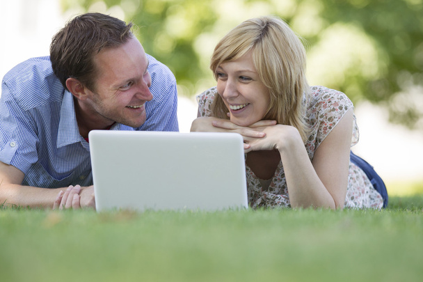 Couple lying on grass with laptop in park - Photo, Image