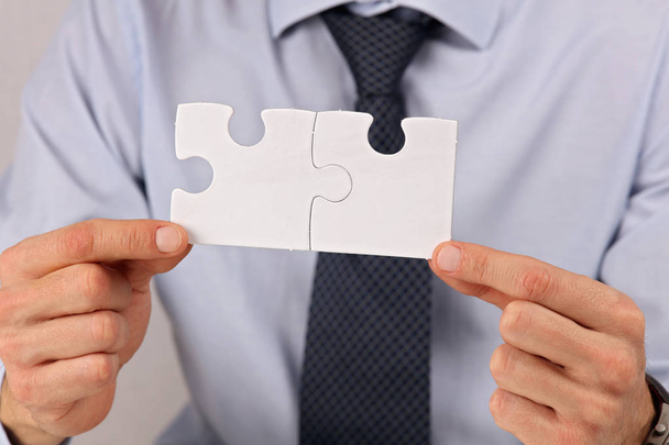 Бизнес-решения, концепция партнерства. Бизнесмен держит в руках два кусочка головоломки
 - Фото, изображение