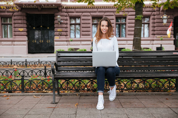 Mujer feliz sentado en el banco y el uso de la computadora portátil al aire libre
 - Foto, imagen
