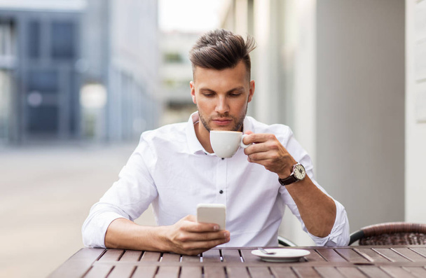 man with smartphone drinking coffee at city cafe - Фото, зображення