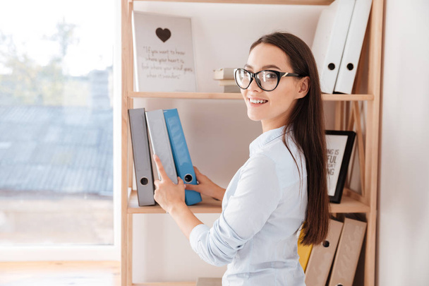 Businesswoman taking folder from book shelf - Fotografie, Obrázek