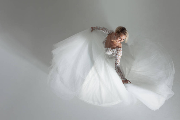 Beautiful attractive bride in wedding dress with long full skirt, white background, dance and smile, top view - 写真・画像