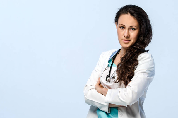 Portrait of a young woman doctor. She is wearing a green scrubs and a white coat. - Photo, Image