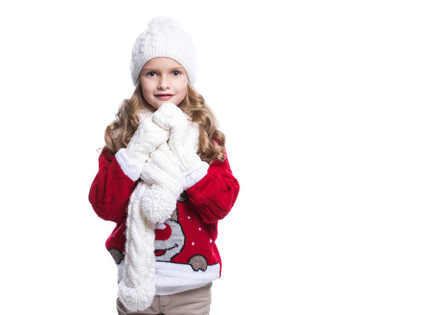 Ładny uśmiechający się mała dziewczynka z kręcone fryzury na sobie sweter sweter, szalik, czapka i rękawiczki na białym tle. Zimowe ubrania. - Zdjęcie, obraz
