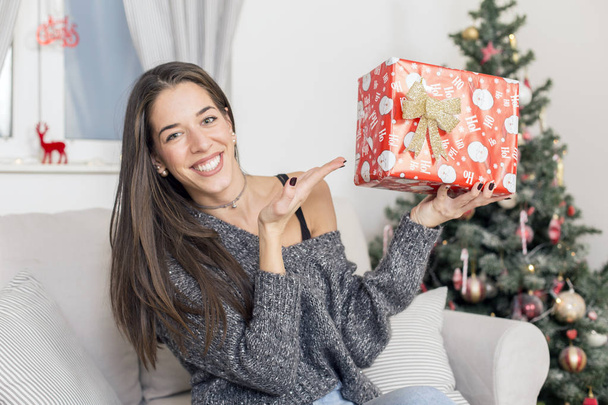 woman next to Christmas tree with with a gift - Фото, изображение