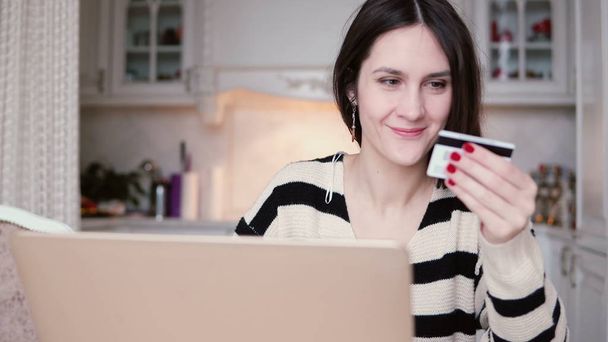Aantrekkelijke jonge lachende vrouw gebruikt kunststof creditcard online winkelen met laptop. Schuif naar rechts - Foto, afbeelding