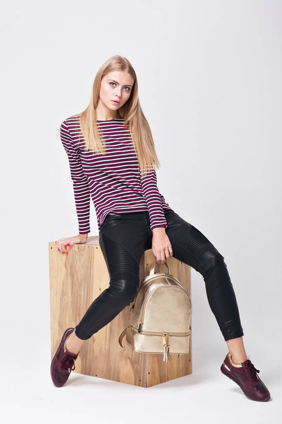 Pretty young girl in sweater striped posing in the studio. Beauty fashion photos. Model sitting on wood box white background. - Valokuva, kuva