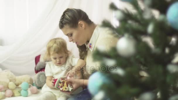 Young mother plays with her baby girl under the Christmas tree. Holiday season. Family time. - Séquence, vidéo