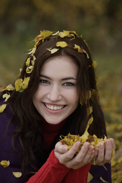 Young woman with fall leaves in hands and hair - Φωτογραφία, εικόνα