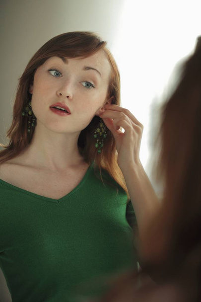 woman trying on earrings in mirror - 写真・画像
