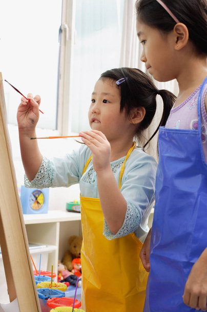 Two girls painting on easel - Foto, afbeelding