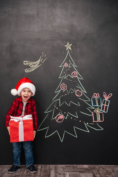 Cheerful child holding gift near Christmas tree drawing on black - Fotó, kép