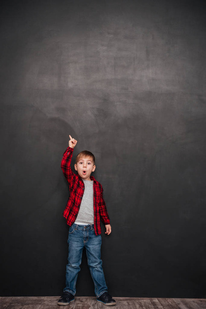Shocked little boy standing over chalkboard and pointing up - Foto, Imagen