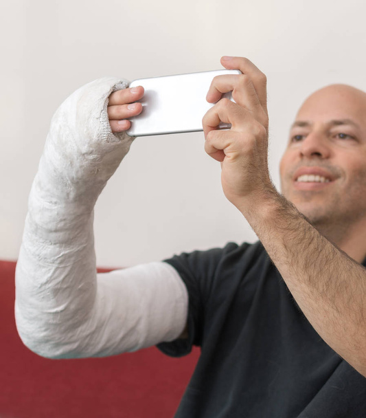 Un joven con un yeso en el brazo tomando una selfie
 - Foto, imagen