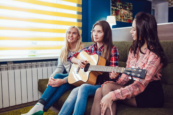 Beautiful girls sitting on couch, have fun and play the guitar in Hostel. - Foto, imagen