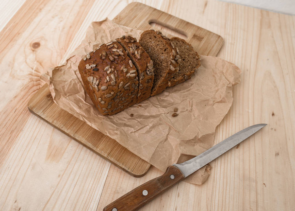 frisches Brot mit Sonnenblumenkernen-Scheibe und Schneidemesser auf rustikalem Tisch - Foto, Bild