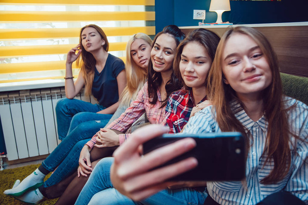 Beautiful girls sitting on the couch, have fun and make selfie in Hostel - 写真・画像